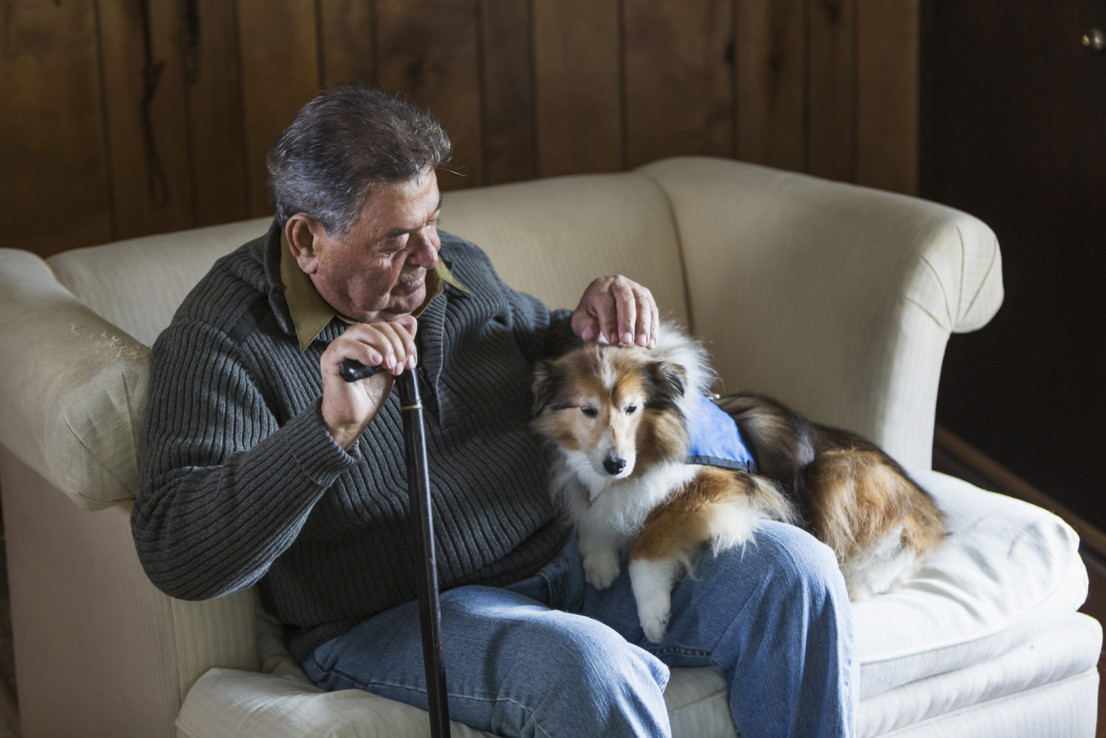 elder man sitting in chair holding a cane with a dog in his lap