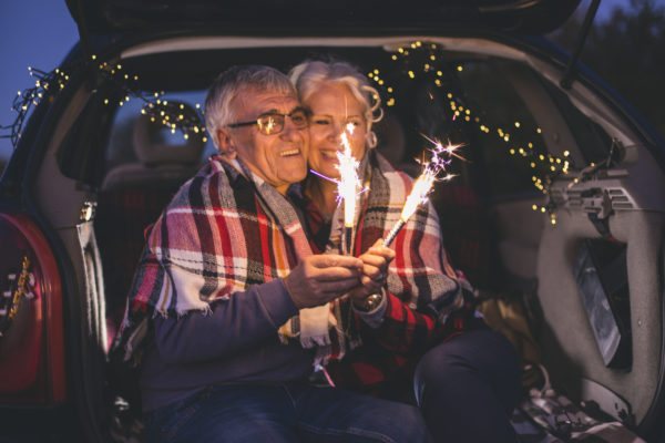 Senior couple sit in open car trunk and hold spark sticks in their hands