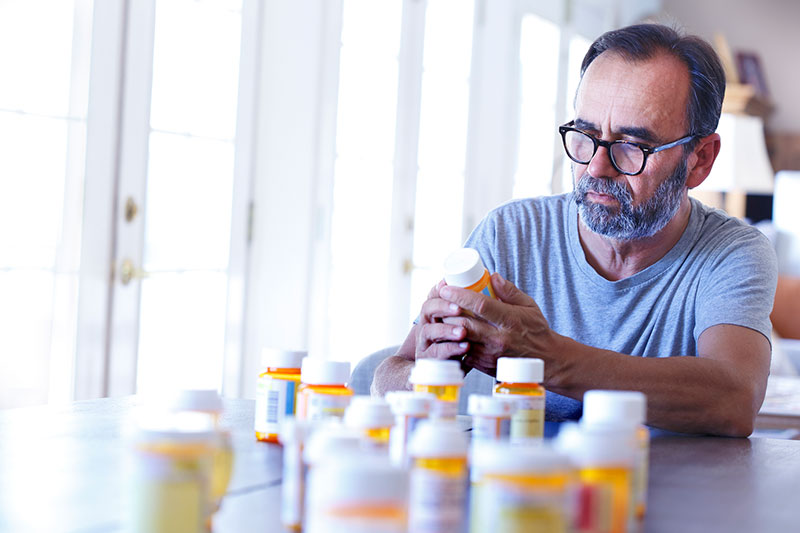 senior man with multiple prescription drug bottles sitting in front of him