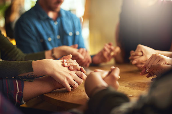 group of people holding hands in prayer around a table