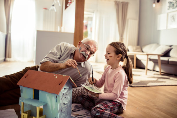 elderly man painting a dollhouse with his granddaughter