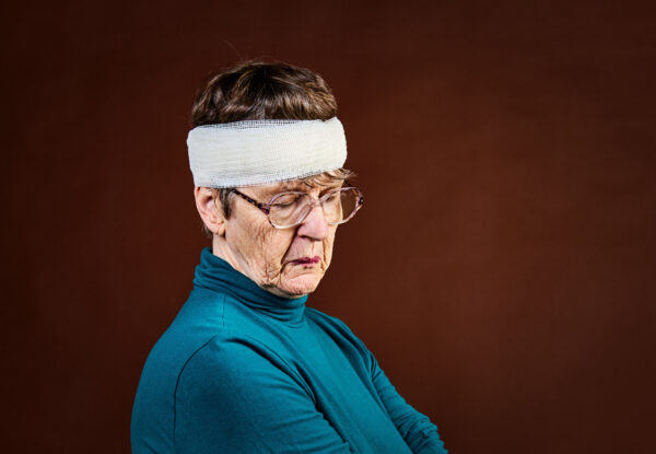 Elderly woman with a bandaged head, looking sad.