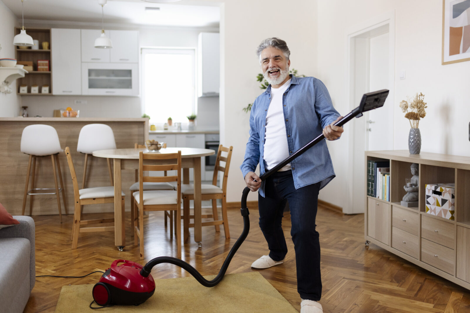 Bearded man dancing happily with a vacuum cleaner, imitating playing the guitar at home